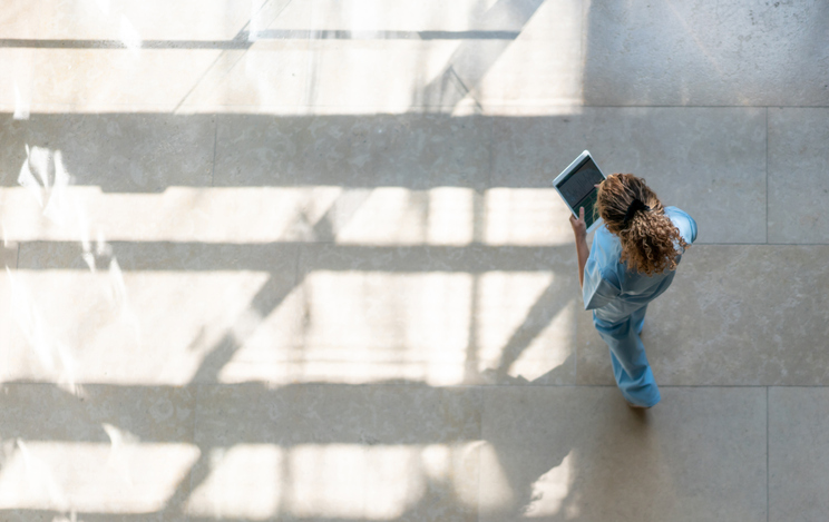 High angle view of nurse walking around hospital while looking at a medical chart on tablet.