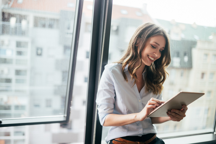Young businesswoman using a digital tablet while standing in front of windows in office